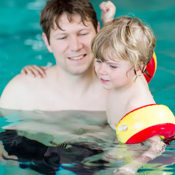 Молодой отец учит своего маленького сына плавать в помещении — стоковое фото