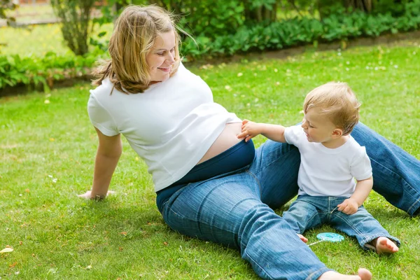 Kobiety w ciąży i śliczny maluch mały syn w ogrodzie. — Zdjęcie stockowe