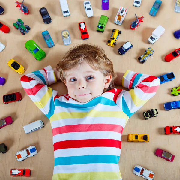 Pequena criança loira brincando com muitos carros de brinquedo interior — Fotografia de Stock