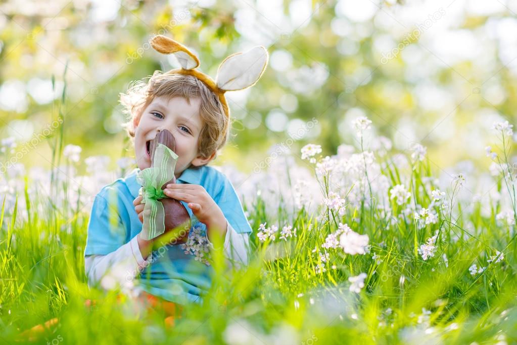 Little kid boy eating chocolate Easter bunny outdoors