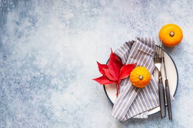 Sonbahar sofrası. Mini dekoratif balkabağı, sonbahar kırmızı yaprakları, açık mavi arka planda çatal ve bıçak. Üst Manzara. Boşluğu kopyala.