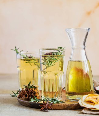 Bardakta armut ya da elma şarabı ve biberiye, tarçın ve taze organik armutla birlikte şişe. Mayalanmış meyve suyu. Hafif beton arka plan. Seçici odak.