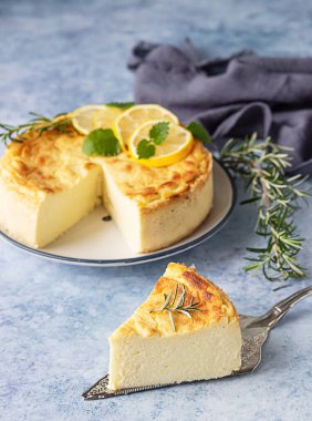 Biberiye, nane ve limon dilimleri ile süslenmiş limonlu peynirli kek. Ricotta peynirli kek ya da güveç yok. Mavi beton arkaplan.