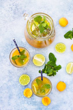 Ev yapımı buzlu limonata ya da olgun kayısı, limon ve naneli çay. Taze kayısı kokteyli ve mavi beton arka planda gözlük. Üst görünüm.