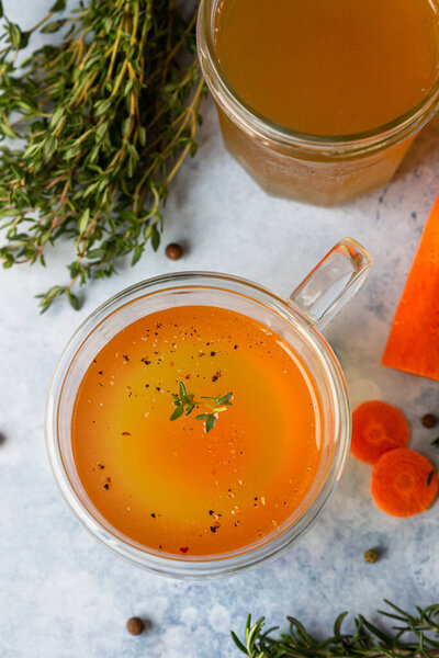 Homemade bone broth in glass mug and vegetables, blue concrete background. Collagen source for the body. Selective focus. Top view.