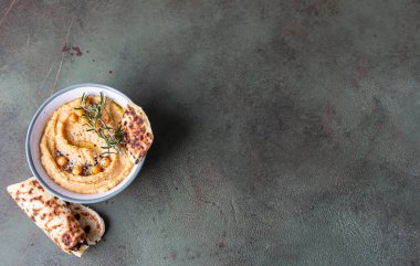 Biberiyeli klasik humus, yassı ekmek, haşlanmış nohut ve zeytinyağı, yeşil taş arka plan. Geleneksel Orta Doğu atıştırması. Seçici odaklanma. Üst görünüm.