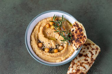 Biberiyeli klasik humus, yassı ekmek, haşlanmış nohut ve zeytinyağı, yeşil taş arka plan. Geleneksel Orta Doğu atıştırması. Üst görünüm.