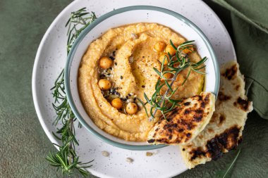 Biberiyeli klasik humus, yassı ekmek, haşlanmış nohut ve zeytinyağı, yeşil taş arka plan. Geleneksel Orta Doğu atıştırması. Üst görünüm.