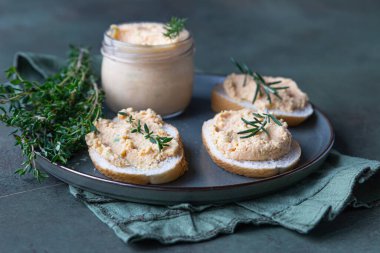 Sandwiches with smoked salmon and soft cream cheese pate or mousse with thyme and rosemary on a ceramic plate, green concrete background. clipart