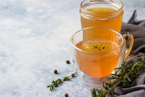 Knochen- oder Gemüsebrühe, Bouillon im Glasbecher und aromatische Kräuter auf blauem Steinhintergrund. Paläo-Diät. — Stockfoto