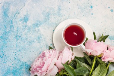 Mavi taştan arka planda bir fincan çay ve pembe şakayık çiçeği. Metin için kopyalama alanı olan üst görünüm. Kadın ya da Anneler Günü hediyesi.