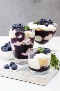 Tiramisu. Yabanmersinli, kremalı, yaban mersinli ve kekikli ev yapımı tatlı. Açık gri arkaplan.