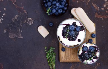 Maskarpone ya da ricotta peyniri, yaban mersini ve bisküvinin koyu arkaplanlı tatlısı. Fırında cheesecake ya da tiramisu yok. Üst görünüm.