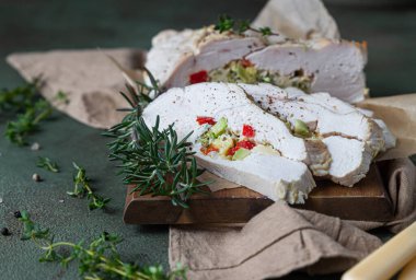 Sebze ve peynirle doldurulmuş hindi göğsü, ahşap kesim tahtasına kekik ve biberiye, yeşil taş arka plan. Seçici odak.