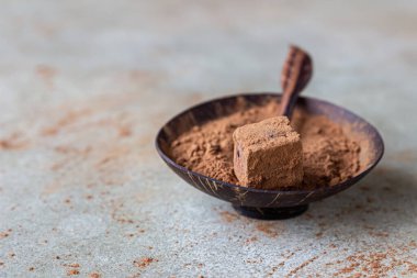 Kakao tozu serpilmiş çikolatalı trüf mantarı ve tahta kasede kakao tozu, açık beton arka plan. Seçici odak.