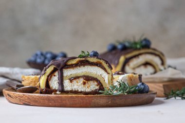 Çikolata kaplı krem peynirli sünger kek rulosu, parşömen üzerinde yaban mersini ve biberiye, açık beton arka plan. Bisküvi İsviçre böreği..