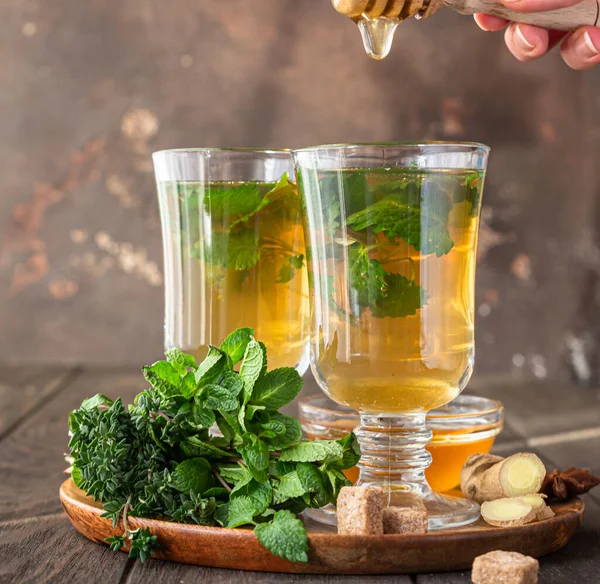 Warmes Kräutergetränk in Gläsern für kalte Tage. Zwei Tassen Ingwertee mit Minze, Thymian und Honig auf einem Holztisch. — Stockfoto