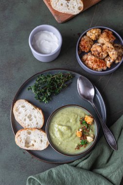 Brokoli kremalı çorba kekik, krema, kavrulmuş karnabahar ve yeşil beton zemin üzerinde taze ekmek. Sağlıklı vejetaryen gıda konsepti. Üst Manzara. Seçici odak.