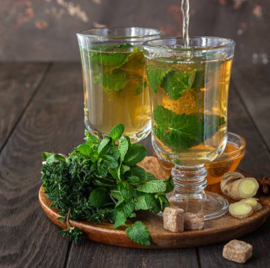 Çay demleme işlemi. Sıcak bitkisel ya da naneli çay, taze bitkiler, zencefil ve bal, ahşap arka plan. Seçici odak.