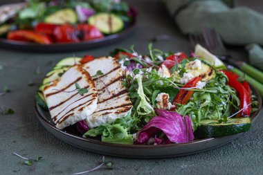 Izgara halloumi peynirli salata, ızgara sebze ve yeşil karışık salata yaprakları, yeşil beton arka plan. Vejetaryen gıda konsepti. Seçici odak.