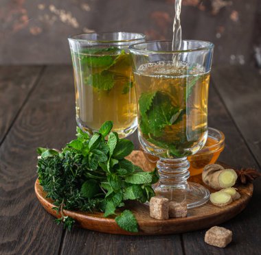 Çay demleme işlemi. Sıcak bitkisel ya da naneli çay, taze bitkiler, zencefil ve bal, ahşap arka plan. Seçici odak.