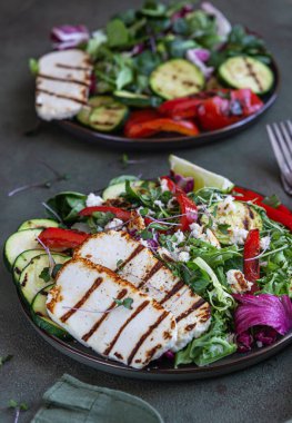 Izgara halloumi peyniri ızgara sebze ve yeşil salata, yeşil beton arka plan. Sağlıklı gıda konsepti. Seçici odak.