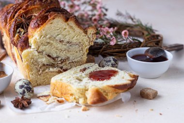 Tarçınlı babka ya da reçelli brioche ekmeği. Paskalya arkaplanı, bıldırcın yumurtaları, çiçekler ve el yapımı dal çelenkleri. Tarçınlı ekmek. Seçici odak.