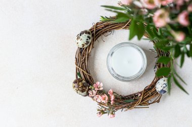 Bahar kompozisyonu, çiçekli dallı çelenk, bıldırcın yumurtası ve mum. Paskalya çelengi ya da rattan bir yuva. Yaratıcılık. Seçici odaklanma. Üst görünüm.
