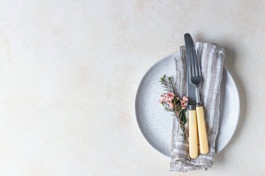 Romantik ya da bahar sofrası. Bıçak ve çatal, küçük pembe çiçekler ve tabakta keten peçete, açık beton arka plan. Düz yatıyordu. Seçici odak.