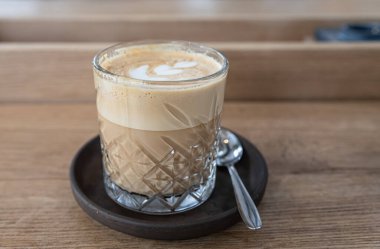 Kafedeki ahşap masada kapuçinolu cam bardak. Seçici odak.