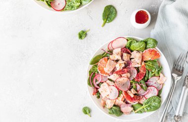 Somon, ıspanak, turp ve portakal sosuyla servis edilen kırmızı portakallı taze salata, açık beton arka plan. Seçici odaklanma. Üst görünüm.