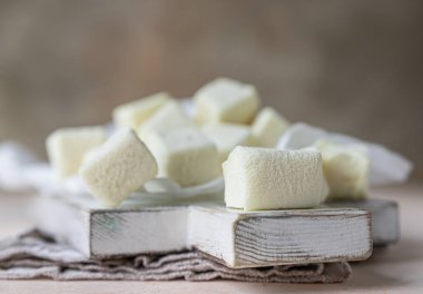 Ahşap kesim tahtasında sarı kare şekilli marşmelov, açık beton arka plan. Seçici odaklanma. Kapat..