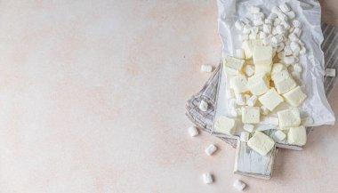 Sarı kare şekilli marşmelov ve beyaz vanilyalı marşmelov tahta kesim tahtasında, açık beton arka planda. Seçici odaklanma. Yüksek anahtar. Üst görünüm.