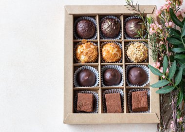 Hafif beton arka planda çeşitli çikolatalar ve pembe çiçeklerle bir hediye kutusu. Üst Manzara. Seçici odak.