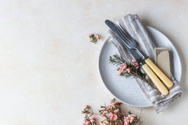 Romantik ya da bahar sofrası. Bıçak ve çatal, küçük pembe çiçekler ve tabakta keten peçete, açık beton arka plan. Düz yatıyordu. Seçici odak.
