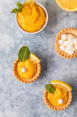 Limonlu mini tartlar, mini kremalı, limon dilimleri ve mavi beton arka planda naneli. Üst Manzara. Seçici odak.