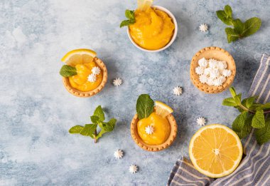 Limonlu mini tartlar, mini kremalı, limon dilimleri ve mavi beton arka planda naneli. Üst Manzara. Seçici odak.