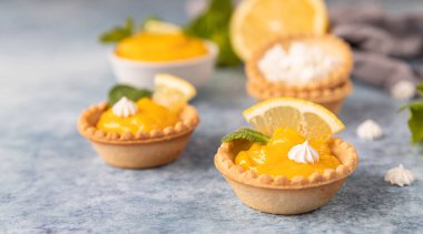 Limonlu mini tartlar, mini kremalı, limon dilimleri ve mavi beton arka planda naneli. Seçici odak.