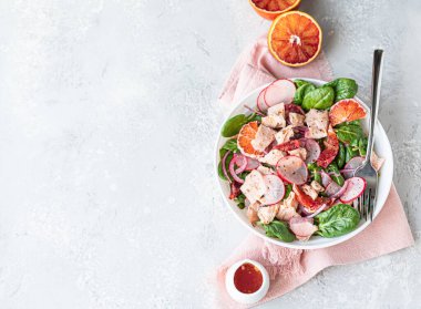 Somon, ıspanak, turp ve portakal sosuyla servis edilen kırmızı portakallı taze salata, açık beton arka plan. Seçici odaklanma. Üst görünüm.