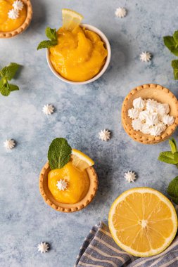 Limonlu mini tartlar, mini kremalı, limon dilimleri ve mavi beton arka planda naneli. Üst Manzara. Seçici odak.