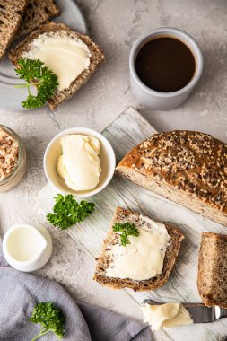 Tereyağlı ve ezmeli taze pişmiş çoklu tahıllı ekmek. Kahveyle kahvaltı, dilimlenmiş ekmek, tereyağı ve ciğer ezmesi. Açık gri arkaplan. Üst görünüm.