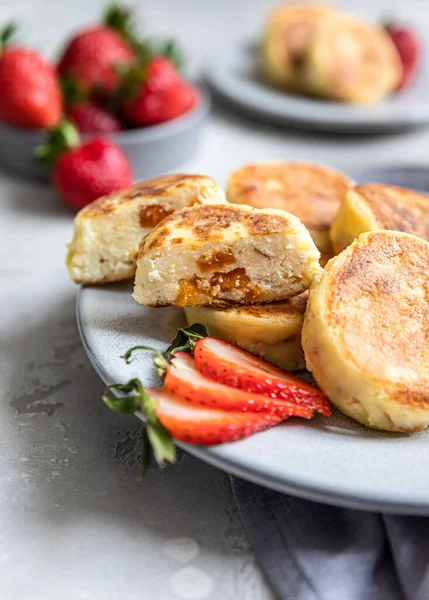 Süzme peynirli krep ya da çilekli börek ve açık gri taşlı arka planda doğal yoğurt. Sağlıklı kahvaltı ya da öğle yemeği. Syrniki..