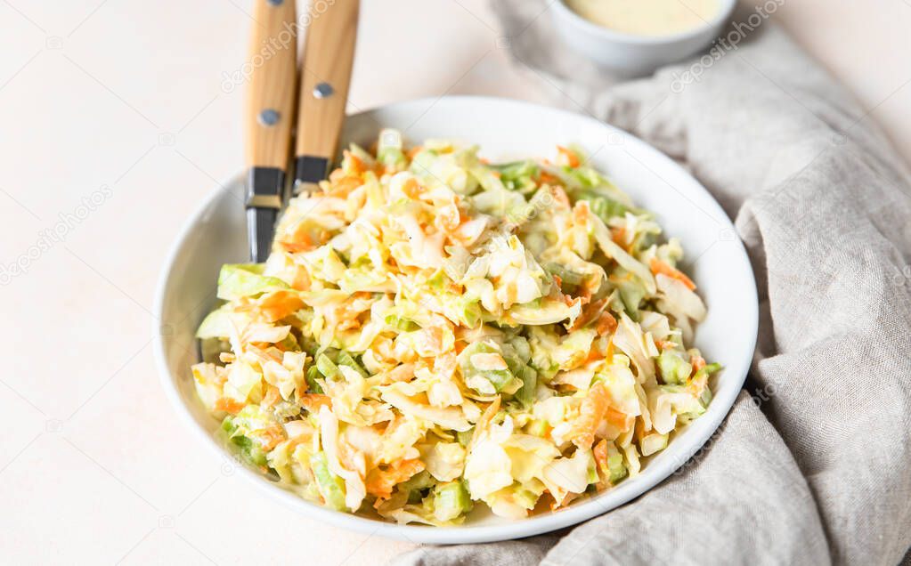 Coleslaw. Salad made of shredded white cabbage, grated carrot and rhubarb with orange mayonnaise dressing in white bowl, light concrete background.