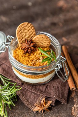 Cam kavanozda, biberiye, anason ve koyu kahverengi arka planla süslenmiş kremalı cam bir tatlı. Peynirli kek, çerez ya da puding yok..