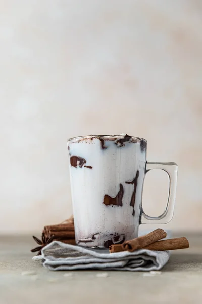 Glazen beker met warme chocolademelk of cacao drank en kaneelstokjes met anijs, lichte betonnen ondergrond. — Stockfoto