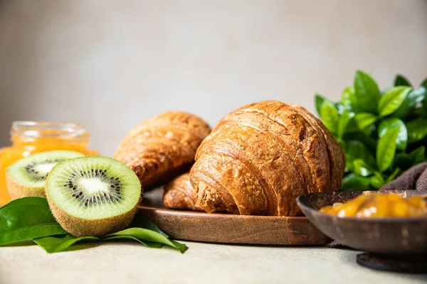 Ropogós croissant narancslekvárral, gyümölcslével és kivivel reggelire. Finom reggeli egy könnyű betonasztalon. — Stock Fotó