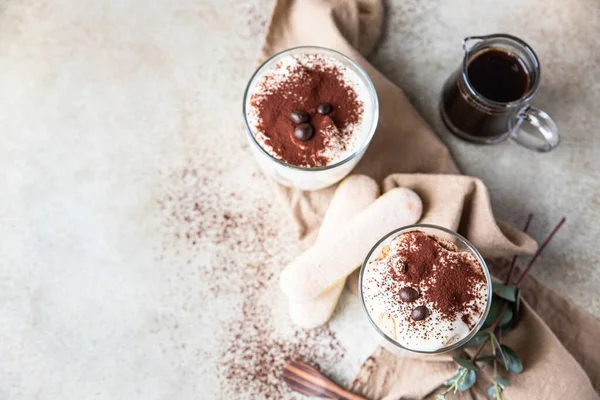 Traditionele Italiaanse dessert tiramisu in glas, licht stenen achtergrond. Koffie smaak portie dessert gemaakt van lieveheersbeestjes en mascarpone versierd met cacao poeder. Bovenaanzicht. — Stockfoto