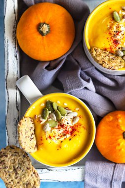 Sıcak ve baharatlı balkabağı çorbası tohumlu, kremalı ve çok tahıllı sağlıklı krakerler ve mavi taşlı arka planda taze balkabağı. Geleneksel sonbahar ve kış yemekleri. Üst görünüm.