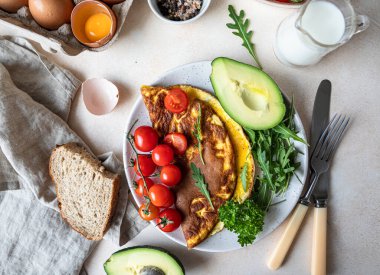 Avokado, vişneli domates ve seramik tabakta roka ile servis edilen omlet. Sağlıklı ve lezzetli keto kahvaltısı veya brunch. Ketojenik diyet.