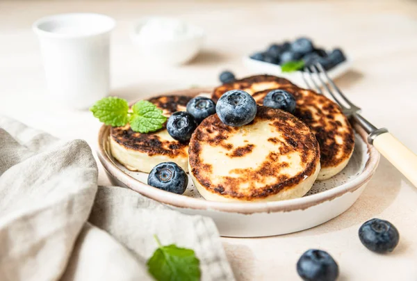 Panqueques de requesón fritos o buñuelos con arándanos y crema agria en un plato. Libre de gluten. Desayuno tradicional de cocina ucraniana y rusa. — Foto de Stock